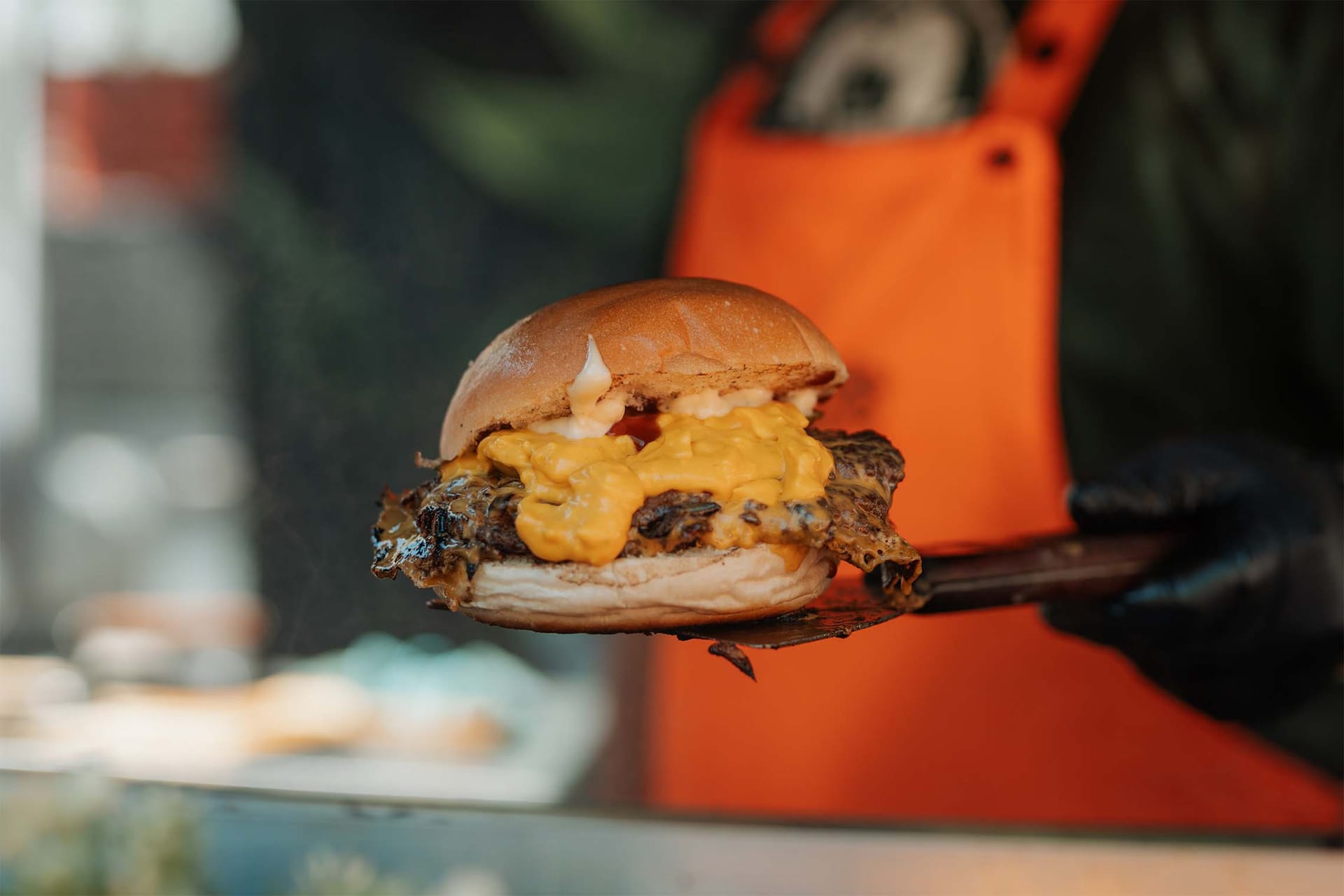 Hamburger s sirovo omako na lopatici, oseba v oranžnem predpasniku