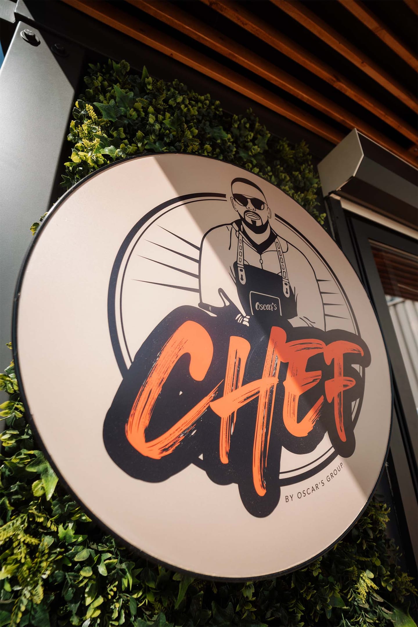 Okrogel napis z ilustracijo kuharja in napisom Chef, obdan z zelenjem.